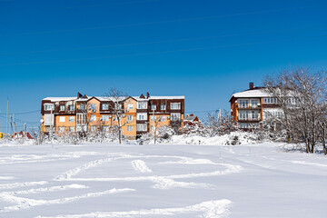 Multi-storey residential buildings made of white and red brick with plastic Windows, stand in winter under a layer of white lush snow in frosty Sunny weather.