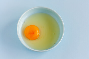 Fresh organic raw yolk and white of egg in light blue bowl on pastel background. Healthy breakfast and fresh ingredients. Selective focus. Top view. Space for text.