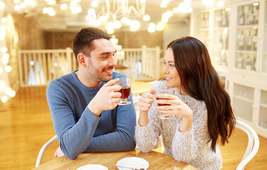 people, communication and dating concept - happy couple drinking tea at cafe or restaurant over festive lights background