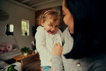 Playful mother and daughter tickling each other while relaxing at home