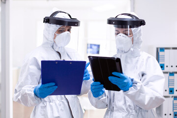 Doctors taking notes wearing ppe suit and face mask in hospital Medical colleagues wearing professional gear against infection with coronavirus as safety precauition.