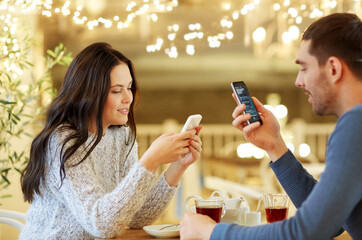 people, communication and dating concept - happy couple with smartphones drinking tea at cafe or...