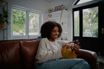 Happy woman relaxing on comfortable couch using smartphone browsing social media