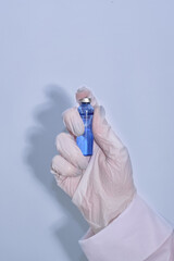 A hand in a medical glove holds an ampoule with a vaccine against the coronavirus infection COVID-19 on a white background. Vaccine. Ampoule with medicine. Doctor holds an injection drug in his hand.