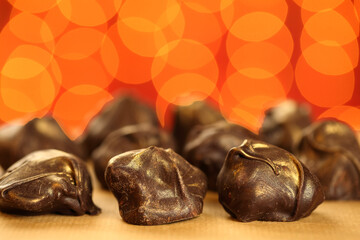 Close up of delicious and healthy homemade raw chocolate bonbons with golden sprinkles against red background with festive lights bokeh