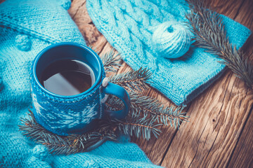 Obraz na płótnie Canvas handmade blue sweater, warm knitted hat, hot cup of tea, Christmas tree and New Year's decor, on an old wooden background