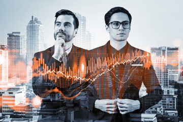 Fototapeta premium Two entrepreneurs in suits pondering about new venture capital and hi-tech start up and try to forecast risks and estimate prospective earning growth. Hologram chart on Bangkok background.