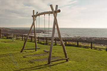 Two children's swings in a park by the seaside, at Crail, Fife, Scotland. The swings are empty, ready for the next two children to have some fun.