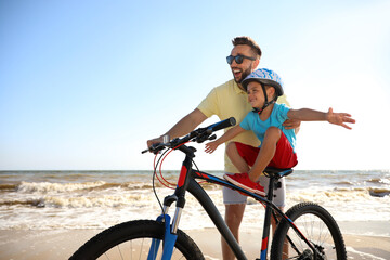 Happy father teaching son to ride bicycle on sandy beach near sea