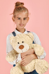 cute little girl is hugging a teddy bear on pink background