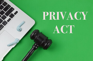 Top view of laptop, earphones and judge gavel over green background written with text PRIVACY ACT. 