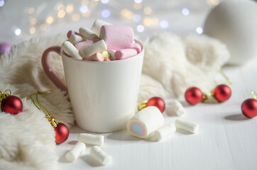 Cup with marshmallows, white ball and red balls on white table.