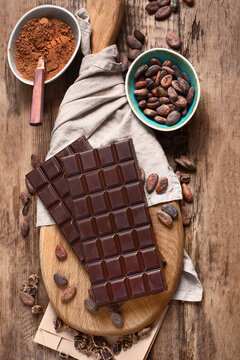 Bars of chocolate, cacao powder and cacao beans on wooden board