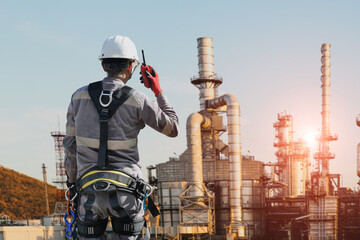 Workers standing wearing full safety harness and operate walkie talkie on oil refinery plant background.