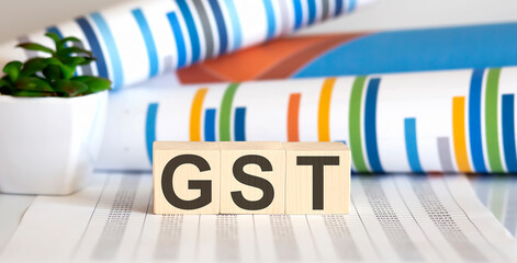 GST written on a wooden cube in front of a charts