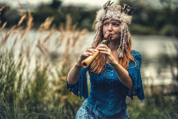 beautiful shamanic girl playing on shaman flute in the nature. © jozefklopacka