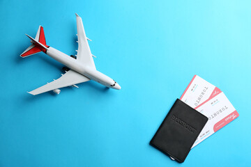 Toy airplane and passport with tickets on light blue background, flat lay