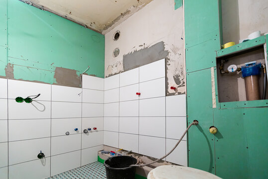 Bathroom with unfinished tiled walls before installing shower and sink, is in the apartment that is under construction, remodeling, renovation, overhaul, extension, restoration and reconstruction. 