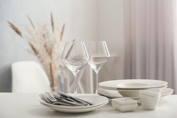 Fototapeta na wymiar Set of clean dishware, wineglasses and cutlery on white table indoors