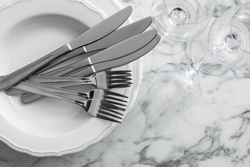 Plates with cutlery and glasses on white marble table, top view