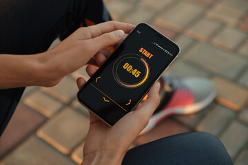 Young woman using fitness app on smartphone outdoors, closeup