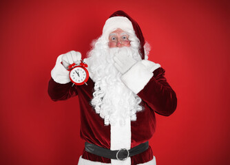 Santa Claus holding alarm clock on red background. Christmas countdown