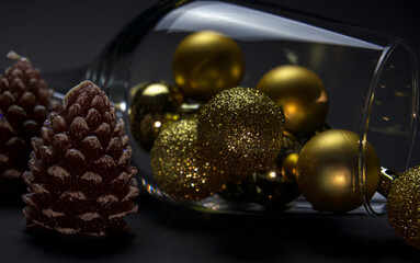  a glass with beautiful golden balls lies on a black background. next to it are two cone-shaped candles. close-up. filmed under artificial light