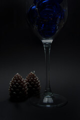 New Year's attributes - two candles in the shape of cones and a beautiful New Year's ball are standing near a glass filled with blue Christmas balls on a black background. filmed under artificial ligh