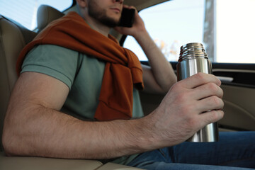 Naklejka premium Man with thermos talking on phone in car, closeup