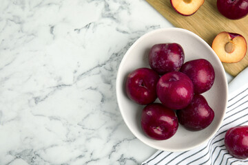 Delicious ripe plums in bowl on white marble table, flat lay. Space for text
