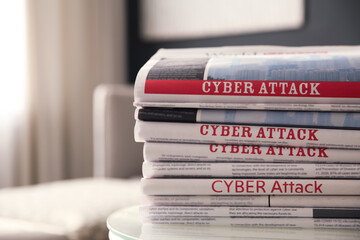 Stack of newspapers with headlines CYBER ATTACK on table indoors, closeup