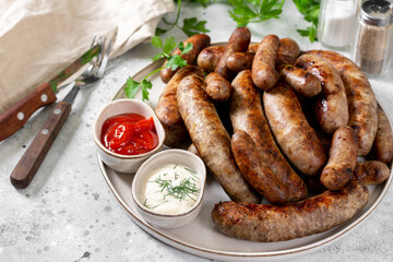 Fried sausages. Bavarian and Nuremberg sausages with spices, sauce, tomatoes and parsley. Delicious meat sausages in a white ceramic plate on a light gray table. German dish