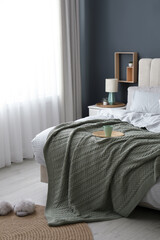 Comfortable bed with knitted green plaid in stylish room interior