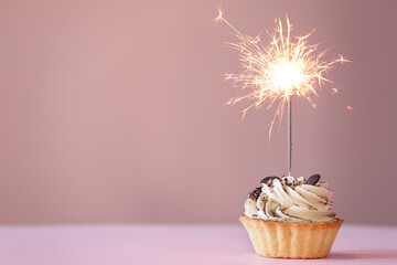 Cupcake with burning sparkler on pink background. Space for text