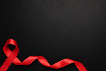 Top view of red ribbon on black background, space for text. AIDS disease awareness