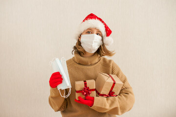 a girl in a santa hat and a medical protective mask holds gifts in her hands. New Year 2021