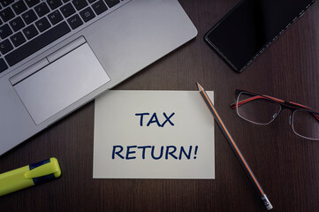 Tax return card. Top view of office table desktop background with laptop, phone, glasses and pencil with card with inscription tax return.  Business concept.