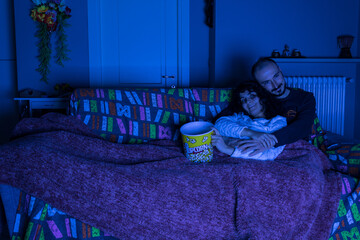 Coppia ragazza e ragazzo seduti sul divano e coperti con un plaid guardano in tv un film in...