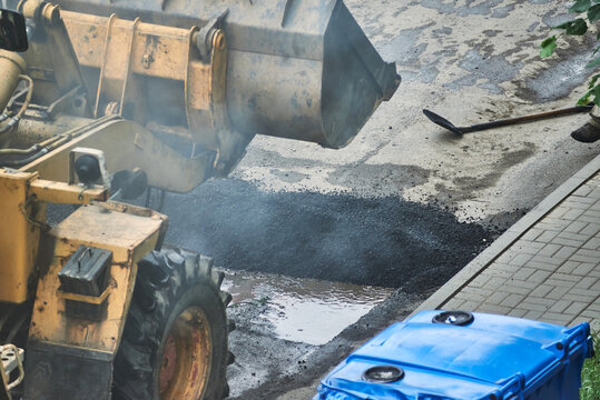 hot smoking asphalt excavator ejects from the bucket. paving with a tractor
