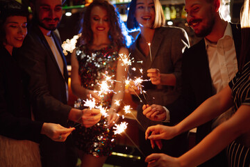 Sparkling sparklers in the hand. Group of happy people holding sparklers at the party. Young friends clinking glasses of champagne  in a nightclub. Celebration, people and holidays concept.
