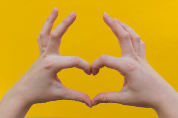 Close-up women's hands make the shape of the heart, on a yellow background. Horizontal photo.