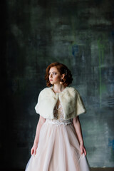 Portrait of red haired girl wearing wedding dress against a white studio background.