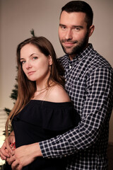 Portrait of a young beautiful couple of a man and a woman in a room. New year and Christmas celebrations. The beige wall. Green Christmas tree.