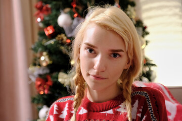 Portrait of a beautiful young blonde woman with two braids, looking at the camera. Christmas sweater. Christmas and new year celebrations.