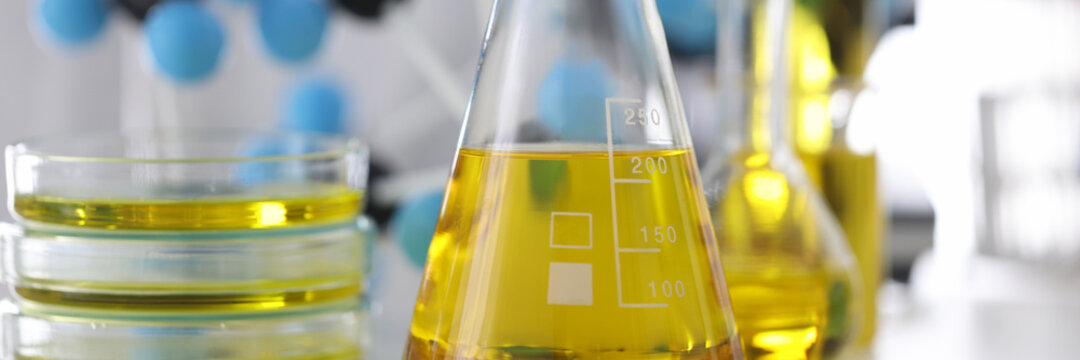 Scientist in rubber gloves holds glass flask with yellow liquid in chemical laboratory closeup. Checking quality of engine oils concept.