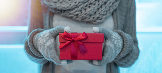 Merry Christmas background banner panorama - Close-up of young woman with gloves and scarf holding a red gift box in her hands