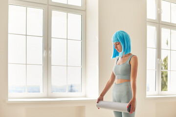 Girl with blue hair or wig standing with fitness carpet in hands ready for workout