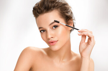 Naklejka premium Young girl using brush for eyebrows. Photo of girl with perfect makeup on white background. Beauty and skin care concept