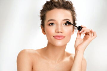 Naklejka premium Woman applies black mascara on her eyelashes. Photo of woman finishing her makeup on white background. Beauty concept