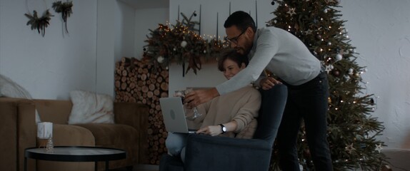 Interracial couple having a video call with friends or family on Christmas eve at home. Holidays celebration during COVID-19 Coronavirus isolation lockdown. New normal concept